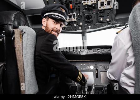 pilota bearded in cap sorridendo e guardando la macchina fotografica vicino co-pilota in simulatore di aeroplano Foto Stock
