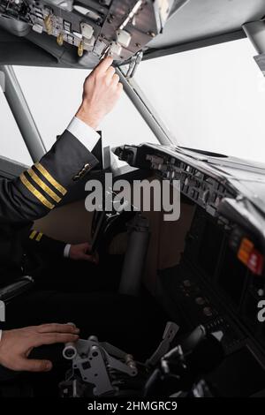 vista ritagliata del pilota in un pannello superiore che raggiunge in modo uniforme vicino al co-pilot utilizzando la leva di spinta nel simulatore di aeroplano Foto Stock