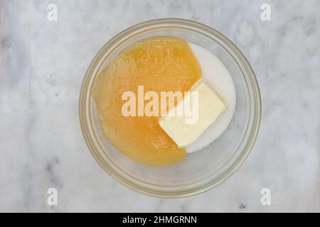 Vista dall'alto di zucchero, burro e miele in una ciotola di vetro come ingredienti di dolce medovik su sfondo di marmo Foto Stock