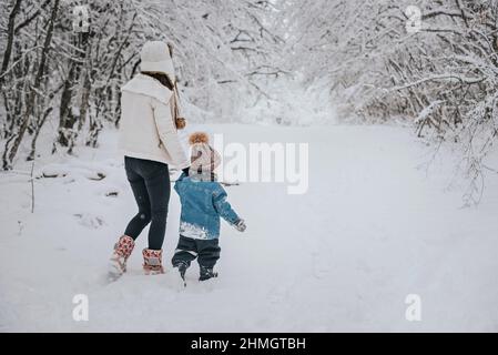 Mamma e figlio camminano nella neve nella foresta. Foto Stock