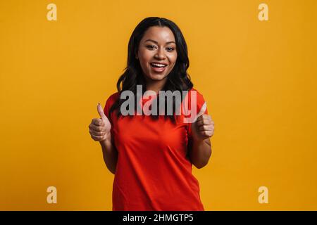 Donna casual africana felice di mezza età in piedi su sfondo giallo parete Foto Stock