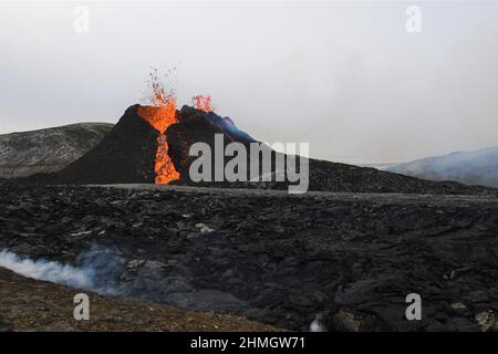 Bocca eruttiva all'eruzione vulcanica di Fagradalsfjall, Islanda. La lava nera crosta è in primo piano e il vapore aumenta. Foto Stock