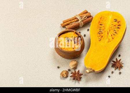 Metà della zucca cruda con purea di zucca di butternut e spezie. Assortimento di ingredienti per la cottura, fondo in pietra e cemento, spazio copia Foto Stock