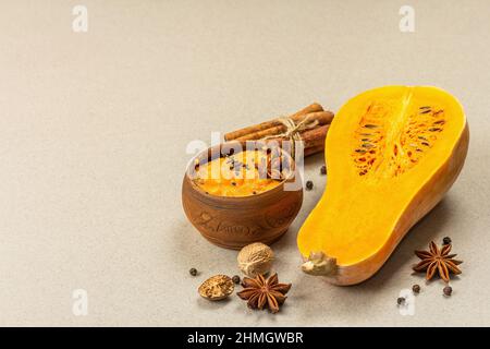 Metà della zucca cruda con purea di zucca di butternut e spezie. Assortimento di ingredienti per la cottura, fondo in pietra e cemento, spazio copia Foto Stock