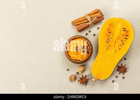 Metà della zucca cruda con purea di zucca di butternut e spezie. Assortimento di ingredienti per la cottura, fondo in pietra, vista dall'alto Foto Stock