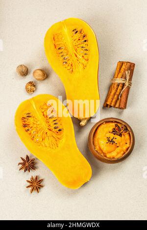 Metà della zucca cruda con purea di zucca di butternut e spezie. Assortimento di ingredienti per la cottura, fondo in pietra, vista dall'alto Foto Stock