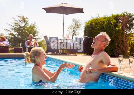 Coppia anziano in pensione che si rilassa in piscina durante la vacanza estiva che si spruzzi a vicenda Foto Stock