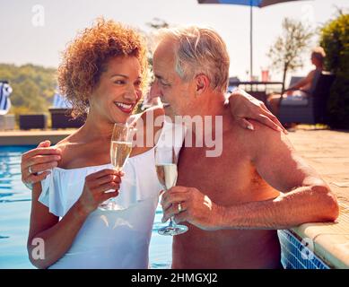 Coppia anziano in pensione che si rilassa in piscina durante la vacanza estiva festeggiando l'apertura di Champagne Foto Stock