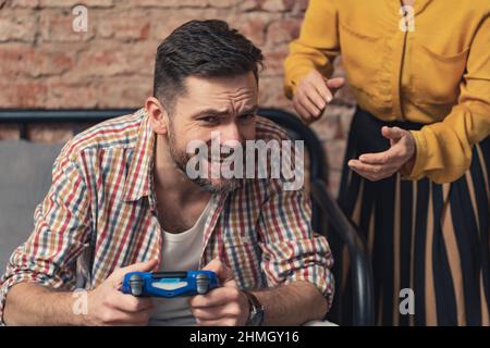 l'uomo caucasico addicted con una barba rifiuta di lasciare andare il pad della console e grida a sua madre anziana. Foto di alta qualità Foto Stock