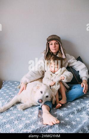 Mamma e figlia coccolano comodamente a casa con il loro animale domestico Labrador Retriever Foto Stock