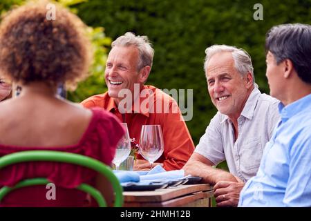 Gruppo di amici maturi che parlano intorno al tavolo al Summer Dinner Party in Garden at Home Foto Stock