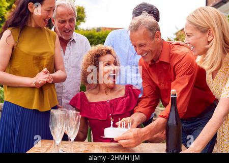 Gruppo di amici maturi a Surprise Birthday Party for Woman in Garden con torta e champagne Foto Stock