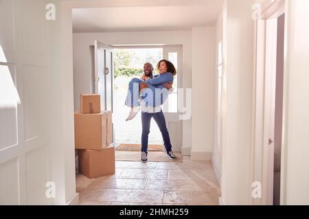 Uomo che porta la donna oltre la soglia come coppia Stand nel corridoio della nuova sede in giorno mobile Foto Stock