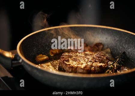 Vista ravvicinata della preparazione dell'hamburger di manzo fatto in casa sulla griglia, con spazio per copiare. Frittura e affumicatura di una succulenta cotoletta in padella con rosmarino e aglio nella cucina del ristorante. Concetto di cibo. Foto Stock