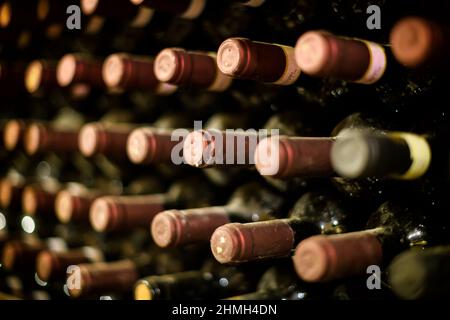 Filari di bottiglie di vino rosso sigillate in foglio che maturano in una cantina su scaffali in un angolo obliquo che si ricava in una enologia, viticoltura e produzione di vino c Foto Stock