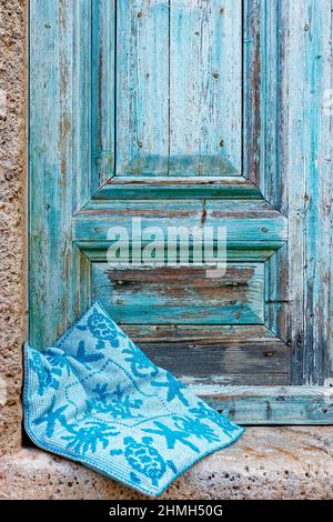 Porta in legno blu con vernice alle intemperie, davanti a essa è presente un cuscino sedile Foto Stock