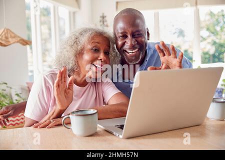 Coppia senior in pensione seduta intorno al tavolo a casa fare videochiamata sul laptop Foto Stock
