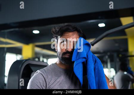 Primo piano colpo di testa di duro lavoro indiano giovane bodybuilder rilassarsi lavando sudore dopo l'esercizio pesante in palestra - concetto sano stile di vita, corpo Foto Stock