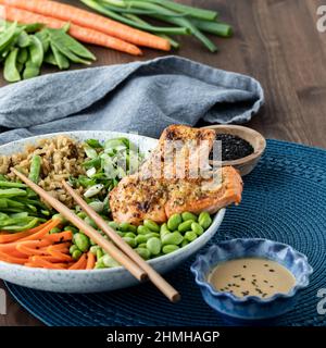 Un'insalata di salmone asiatico sano ciotola con ingredienti freschi in dietro. Foto Stock