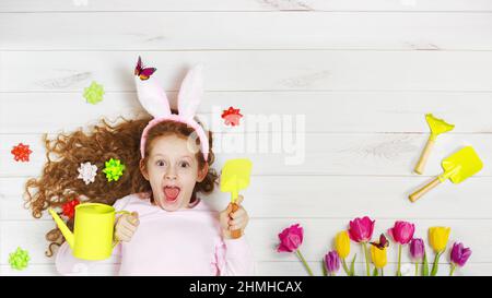 Ragazza che ride in orecchie di coniglio adagiata sul pavimento di legno. Buona Pasqua, giorno delle madri, concetto di infanzia. Foto Stock