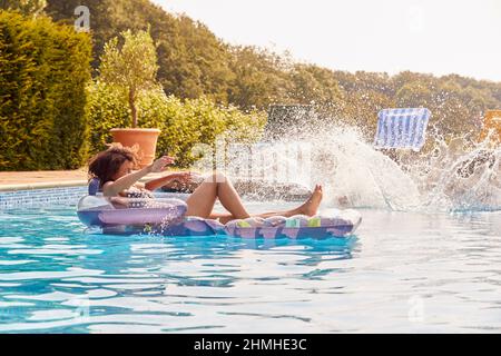 Donna rilassante galleggiamento su gonfiabile in piscina come figlio di Teenage salta in vacanza estiva Foto Stock