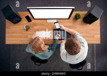 Vista dall'alto di progettisti grafici maschili e femminili che lavorano al computer guardando il telefono cellulare Foto Stock