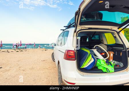 Indietro vista giovane adulto uomo surfer in muta mettere fuori surf bordo kite attrezzatura sulla spiaggia di sabbia da van veicolo con tetto box mare mare spiaggia Foto Stock