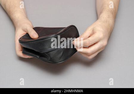 Due mani di un uomo di mezza età aprono una borsa nera su uno sfondo grigio. Un piccolo contenitore chiuso con chiusura lampo. All'interno della stanza. Selettivo per Foto Stock