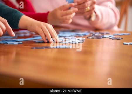 Primo piano di nipoti con nonni sedersi intorno tavolo a casa facendo Jigsaw Puzzle insieme Foto Stock