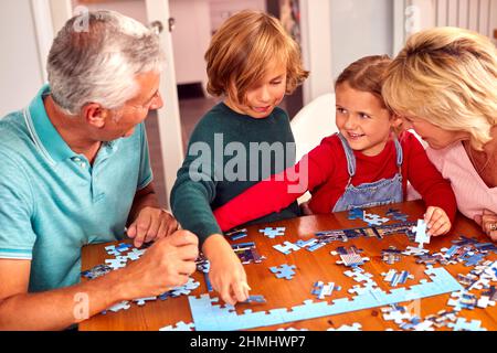 Nipoti con nonni si siedono intorno tavolo a casa facendo Jigsaw Puzzle insieme Foto Stock