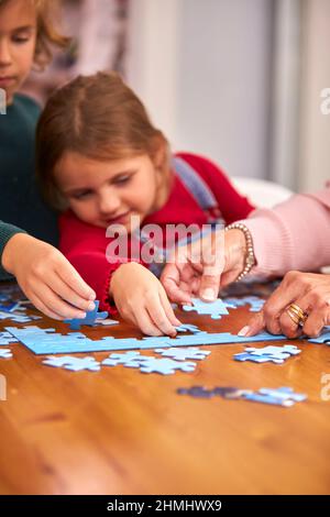 Primo piano di nipoti con nonni sedersi intorno tavolo a casa facendo Jigsaw Puzzle insieme Foto Stock