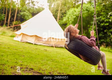 Ragazza che gioca su Tire Swing in giardino a casa con tenda in background Foto Stock