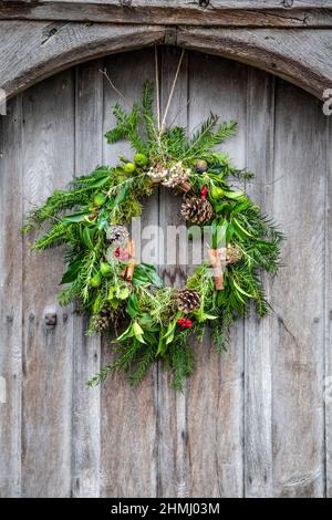 Corona di Natale con coni di pino, foglie e ramoscelli su una porta di legno (Ashwell, Hertfordshire, Regno Unito) Foto Stock