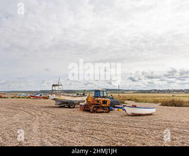Un apripista arrugginito vintage crawler, un trattore e una barca da pesca su una spiaggia di ghiaia, Cley-Next-the-Sea, un villaggio nel nord di Norfolk, East Anglia, Inghilterra Foto Stock