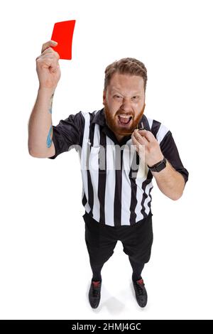 Giovane appassito sportivo arbitro indossare campo giudice uniforme mostrando rosso scheda isolato su sfondo bianco studio. Concetto di sport, regole, competizioni Foto Stock