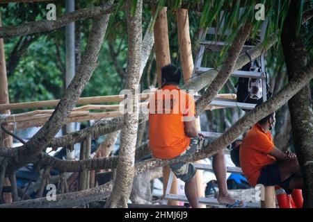bagnino in camicia arancione seduta su albero in spiaggia con turisti in background a havelock swaraj dweep andaman nicobar isole india Foto Stock