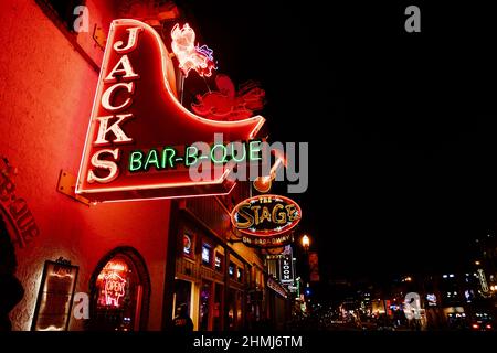 Nashville, Tennessee - 11 gennaio 2022: Cartello al neon Jacks Bar-b-que su Broadway Street, insieme ad altri famosi cartelli, illuminato di notte Foto Stock