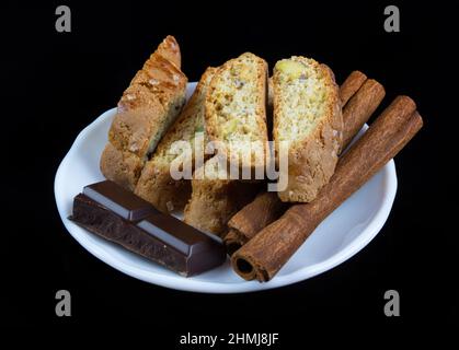 Bastoncini di Cinnanon, cioccolato e bisquits in un piatto bianco isolato su sfondo nero Foto Stock