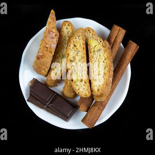 Bastoncini di Cinnanon, cioccolato e bisquits in un piatto bianco isolato su sfondo nero Foto Stock