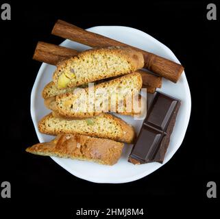 Bastoncini di Cinnanon, cioccolato e bisquits in un piatto bianco isolato su sfondo nero Foto Stock