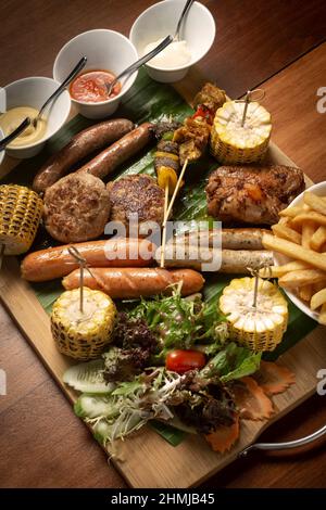 Piatto di carni miste con barbecue con polpette, salsicce, spiedini e ali di pollo su sfondo di legno Foto Stock