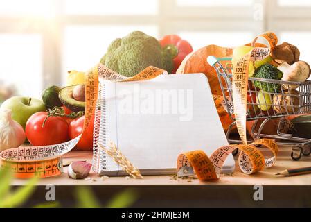 Taccuino vuoto per scrivere ricetta di verdure per il controllo del peso e perdere la pianificazione del peso su un tavolo con nastro di misurazione carrello e vegetab Foto Stock