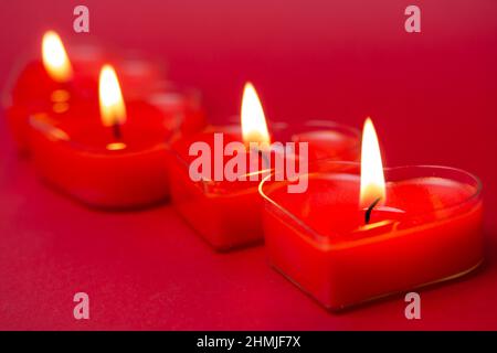 Quattro candele rosse a forma di cuore con fiamme ardenti. Lingue di fuoco su sfondo rosso. San Valentino, passione, amore, sentimenti concetto. Mono Foto Stock