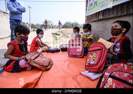 Una classe della scuola elementare sul confine India-Bangladesh è condotta su una strada vuota accanto alla recinzione a Nabin Nagar, nel Bengala occidentale. Il governo del Bengala occidentale ha lanciato “Paray Shikshalaya”, un programma di scolarizzazione basato sulla comunità rivolto agli studenti primari che hanno abbandonato il sistema di istruzione formale negli ultimi due anni a causa della chiusura delle scuole a causa del Covid-19. India. Foto Stock