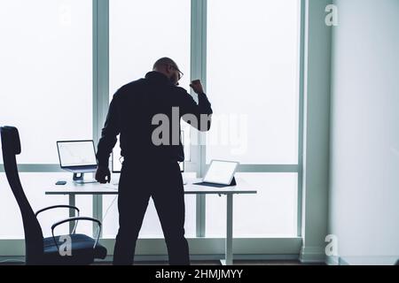 Un uomo d'affari senza volto che alza il pugno nella celebrazione in un ufficio moderno Foto Stock