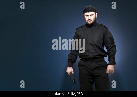 Bodyguard. Una protezione di sicurezza maschile in uniforme nera e un cappuccio hanno preso una posizione protettiva. Difensore. Sicurezza privata. Mercenario. Foto Stock