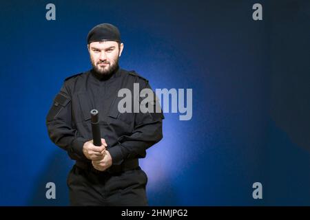 Una guardia maschile in una divisa nera e un cappuccio hanno preso una posizione difensiva, puntando con un guinzetto all'intruso. Bodyguard. Sicurezza privata. Difendete Foto Stock