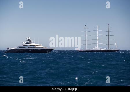 Enorme megayacht a motore e barca a vela sono vicino al porto di Monaco al tramonto, angolo d'acqua vista, megayachts sono ormeggiati in mare, il sole riflessione su lucido Foto Stock