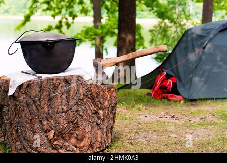 Picnic con tenda. L'ascia e la pentola sono sul molo vicino al fuoco durante il pic-nic sul lago. Foto Stock