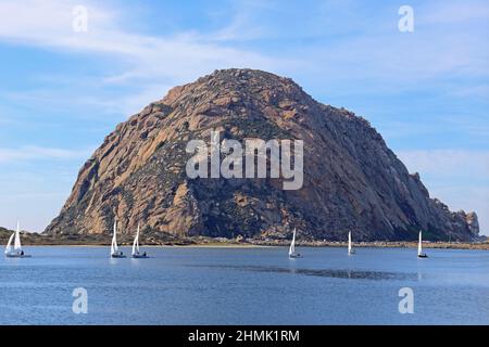 Morro Rock, un'antica spina vulcanica situata a Morro Bay, California, è mostrato durante il giorno, con barche a vela gommoni nel porto. Foto Stock